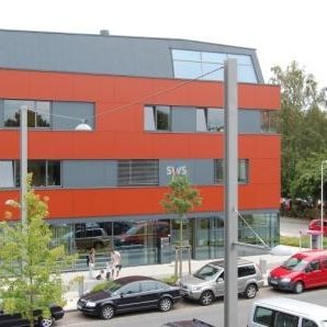 Das moderne Service-Center der Stadtwerke Stralsund mit einer auffälligen roten Fassade, großen Fenstern und geparkten Autos im Vordergrund.