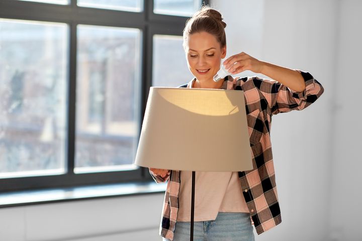 Eine junge Frau richtet eine moderne Stehleuchte ein und scheint das Design ihres Raumes zu überdenken oder zu verändern. Die Kombination aus ihrer lässigen Kleidung und dem stylischen Interieur deutet auf ein gemütliches, aber trendbewusstes Zuhause hin.